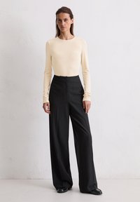 Crème lange mouwen top in combinatie met zwarte pinstripe high-waisted wijde broek. Gladde stof met subtiele textuur en een op maat gemaakte silhouet.
