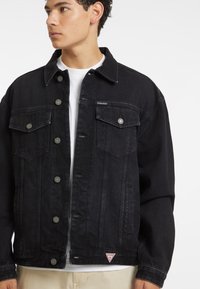 Giubbotto in denim nero con chiusura a bottoni, due tasche sul petto e logo del marchio. Presenta una vestibilità comoda e dettagli in metallo argentato.