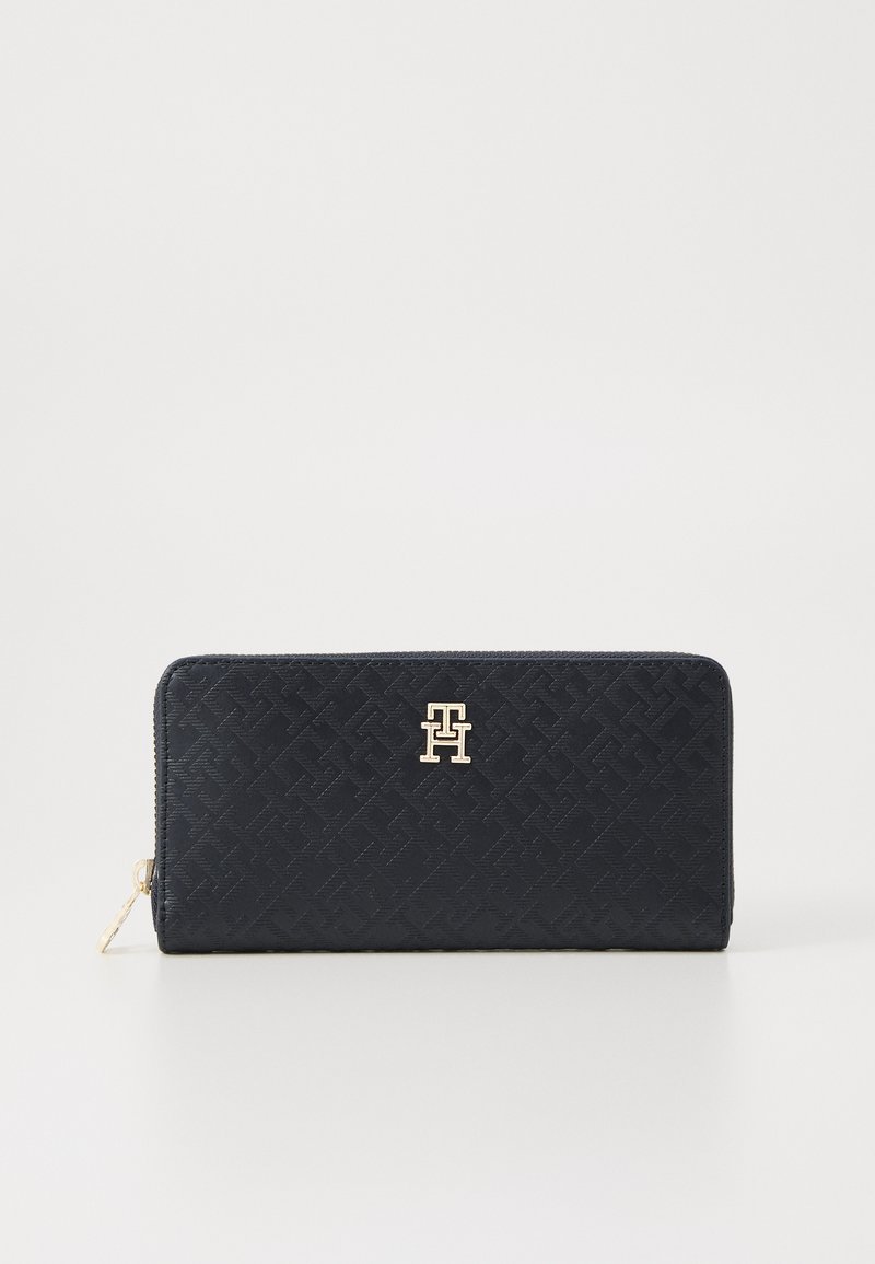 Portafoglio blu navy con un motivo testurizzato, hardware con logo dorato e chiusura con zip. Forma rettangolare compatta progettata per una facile conservazione.