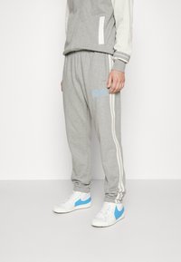Grå sweatpants med vita sidränder, pryds av en ljusblå Nike-logotyp. Kombineras med vita sneakers med blå accenter. Mjuk material, avslappnad passform.
