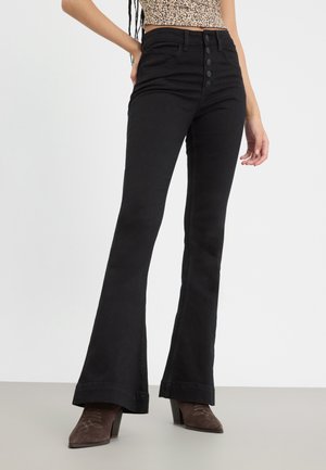 Svarte velourjeans med høy midje, med knappestolpe, fem lommer og en jevn tekstur. Båret med brune hæler støvler.