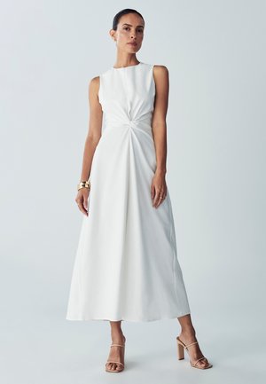 Vestido blanco sin mangas con un detalle frontal trenzado, falda fluida y silueta en A. Tejido ligero y suave. Diseño simple.