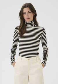 Mustakorvaraitainen turtleneck-paita pitkillä hihoilla, yhdistettynä kermavärisiin housuihin. Rakenteellinen kangas, istuva malli, minimalistischinen tyyli.