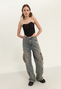 Svart off-shoulder topp med ribbet tekstur kombinert med lysegrå baggy cargo-jeans med sidelommer og en avslappet passform. Svart fottøy fullfører antrekket.