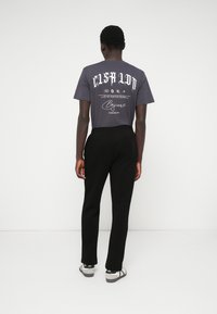 T-shirt cinza de algodão com texto em branco em destaque e designs gráficos nas costas; combinado com calças pretas e sneakers cinza e preto.