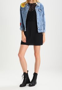 Džínová bunda s květinovými a srdcovými nášivkami, černý krajkový top a krátké černé šaty. Doplněno černými kotníkovými botami na šněrování.