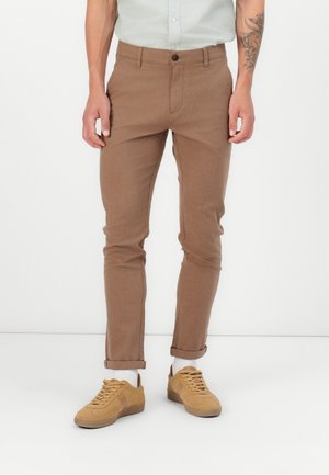 Braune, tapered Hosen aus robustem Stoff, mit einem Knopfverschluss, seitlichen Taschen und umgeschlagenen Säumen, kombiniert mit beige Sneakers.