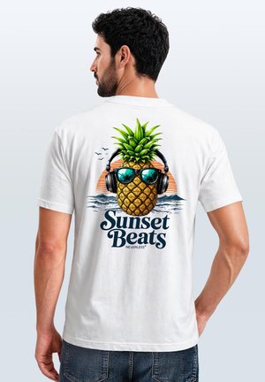 Mann trägt weißes T-Shirt mit buntem Ananas-Motiv, das Sonnenbrille und Kopfhörer trägt, Text "Sunset Beats" und Grafik eines Ozean-Sonnenuntergangs auf dem Rücken.