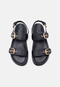 Μαύρα δερμάτινα σανδάλια με δύο ρυθμιζόμενους χρυσούς αγκράφες και λουράκια στον αστράγαλο, επίπεδη σόλα και λογότυπο της μάρκας τυπωμένο στην πάτημα.