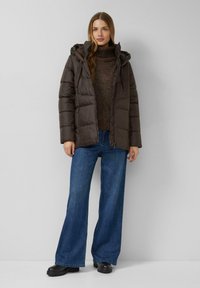 Bruine pufferjas met capuchon, voorzien van een rits aan de voorkant en een doorgestikt ontwerp. Gecombineerd met donkerblauwe wijde jeans en zwarte laarzen.