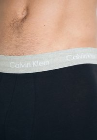 Fekete Calvin Klein boxer alsónadrág, világosszürke, fehér márkanevével ellátott elasztikus derékpánttal. Puha pamut anyag, sima textúrával.