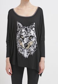 Svart långärmad T-shirt med en stor paljett design av en varg i silver och guld. Rundad halsringning med kontrasterande kant. Mjuk tyg.