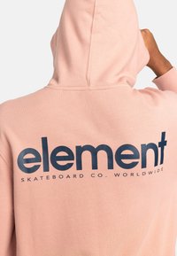 Felpa rosa con un grande logo blu navy sul retro che recita "element SKATEBOARD CO. WORLDWIDE." Tessuto morbido con una vestibilità comoda.