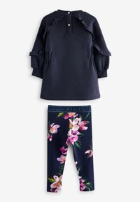 Tumesinine sweatshirt ruffles detallede ja nööpidega, koos lillemustriga retuusidega, millel on roosa ja valge lillemuster tumedal taustal.