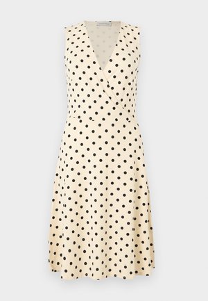 Robe crème sans manches, coupe trapèze, avec des pois noirs et un corsage à encolure en V style cache-cœur.