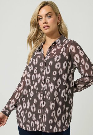 Blondine draagt een losse, lange mouwen, blouse met knopen en een zwart-lichtroze dierenprint.