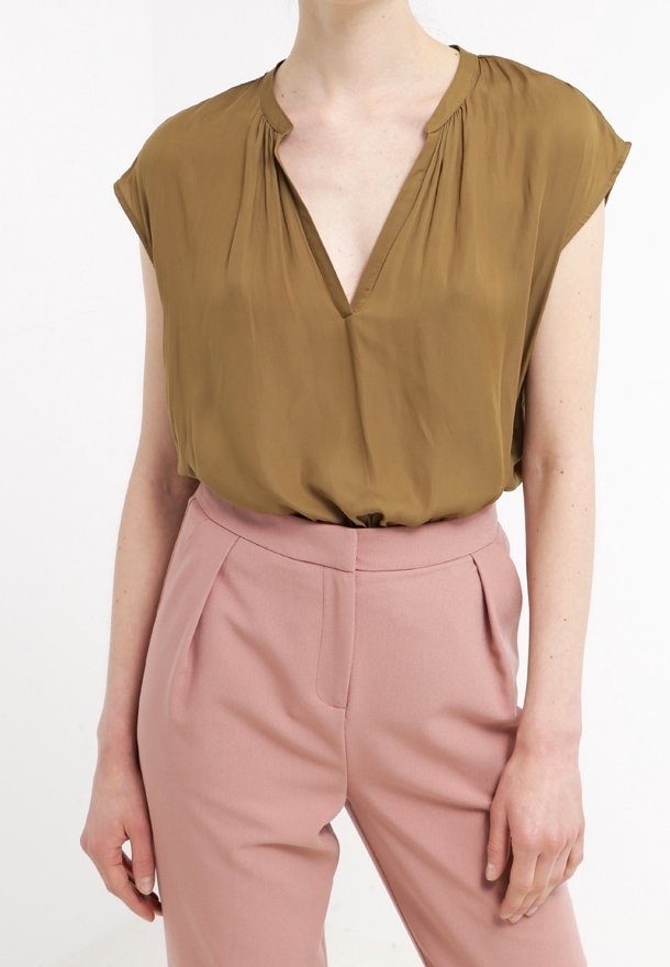 Femme portant un chemisier ample vert olive à manches courtes, rentré dans un pantalon taille haute, sur mesure, rose poudré.