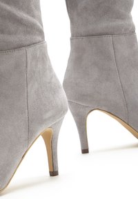Gray suede ankle boots with a pointed toe and 4-inch stiletto heel. Smooth texture and seam detailing on the upper section.