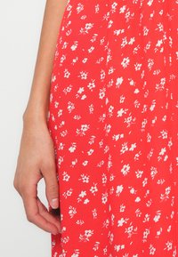 Punane lilleline kleit, mis on valmistatud kergest kangast, millel on hajutatud valged lilled ja rohelised aktsendid. Disain sisaldab peeneid lehti ja sujuvat tekstuuri.