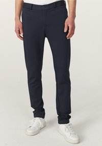 Marineblauwe, slim-fit broek van gestructureerde stof met een knoopsluiting en zijzakken, gedragen met witte sneakers.