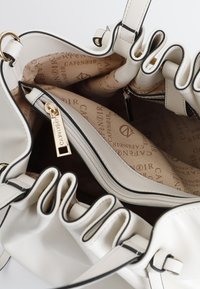 Borsa bianca con un design testurizzato, bordi arruffati e rifiniture nere. L'interno presenta una tasca con zip e rivestimento in tessuto marchiato.