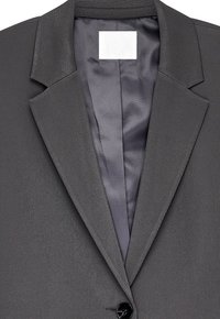 Blazer gris avec un tissu texturé, à revers fins et intérieur en satin. Doté d'une fermeture à un seul bouton et d'une étiquette simple.