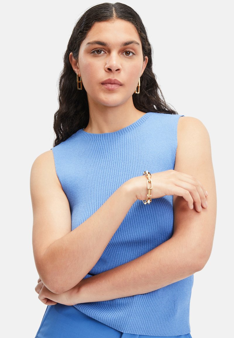 Blaues, geripptes ärmelloses Top mit Rundhalsausschnitt, kombiniert mit einem goldenen Kettenarmband. Der Hintergrund ist schneeweiß.