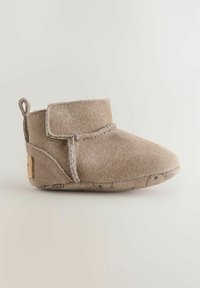 Botte en suède beige avec un bout arrondi, un intérieur doublé et une sangle réglable en Velcro. Dispose d'une semelle texturée avec des motifs subtils.
