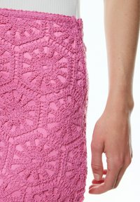 Roze gehaakte rok met ingewikkelde cirkelpatronen en een golvende tailleband, die de textuur van de stof en vakmanschap benadrukt.