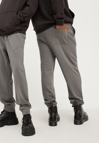 Jogging gris avec des poignets élastiques et une poche arrière, associés à des bottes à plateforme noires avec une semelle proéminente et un design à lacets.