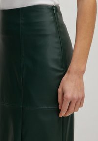 Dunkelgrüner Leder-Bleistiftrock mit glatter Textur, versehen mit einem verdeckten Reißverschluss auf der Rückseite und sauberen Nahtdetails.