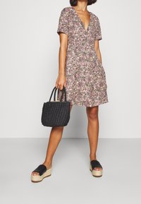 Robe fleurie avec un décolleté en V et des manches courtes, ornée d'un mélange de fleurs roses, jaunes et vertes ; associée à un sac tressé noir et des sandales à plateformes.