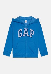 Sweatshirt azul com fecho zip, feito de tecido macio, apresentando um grande logotipo "GAP" em branco e azul-marinho, com dois bolsos frontais e capuz.