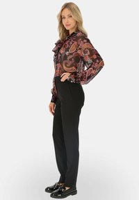 Czarne spodnie zestawione z przezroczystą, wzorzystą bluzką z falbankami i kokardą. Bluzka zdobią wzory paisley w żywych kolorach.
