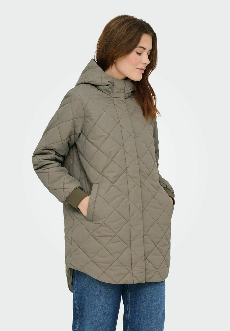 Polnilo z luknjasto kapuco v olivno zeleni barvi, z bočnimi žepi, rebrastimi manšetami in daljšim zadnjim delom. Tkanina z reliefnim vzorcem v obliki diamantov.