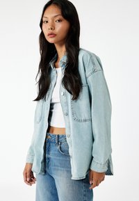 Camicia di jeans leggera color azzurro con chiusura a bottoni frontale, due tasche sul petto e vestibilità leggermente oversize. Abbinata a jeans a vita alta color azzurro chiaro.