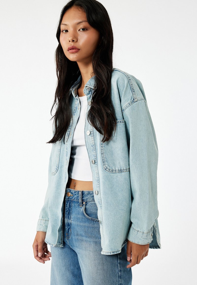 Camicia di jeans leggera color azzurro con chiusura a bottoni frontale, due tasche sul petto e vestibilità leggermente oversize. Abbinata a jeans a vita alta color azzurro chiaro.