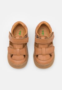 Tan leather shoes with hook-and-loop straps. Open-toe design features cutouts, stitched accents, and a flexible rubber sole.
