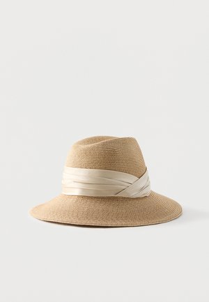 Beige strooien hoed met brede rand met een crèmewit satijnen lint gewikkeld rond de basis van de kroon, getoond op een lichte achtergrond.