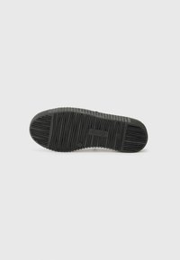 Semelle en caoutchouc noir avec des rainures et des crêtes texturées. Présente un design plat et le nom de la marque "Reebok" embossé sur la surface.