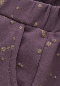 Lila Stoff mit weicher Textur, der mit verstreuten goldenen, glitzernden Punkten versehen ist. Enthält einen gerafften Bund und zwei Seitentaschen.
