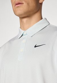 Ανοιχτό γαλάζιο πόλο μπλουζάκι με οριζόντια σχέδια, κουμπωτό γιακά και μαύρο λογότυπο Nike στην αριστερή πλευρά του στήθους. Διαθέτει υφαντή ύφη.