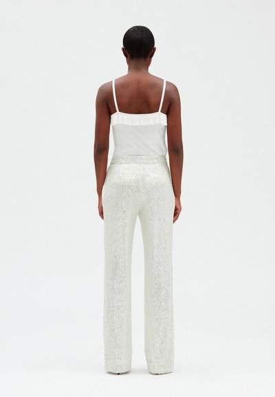 Camisola bianca in rete con spalline sottili e dettaglio arricciato, abbinata a pantaloni argentati a palazzo con paillettes e vita alta, vista da dietro.