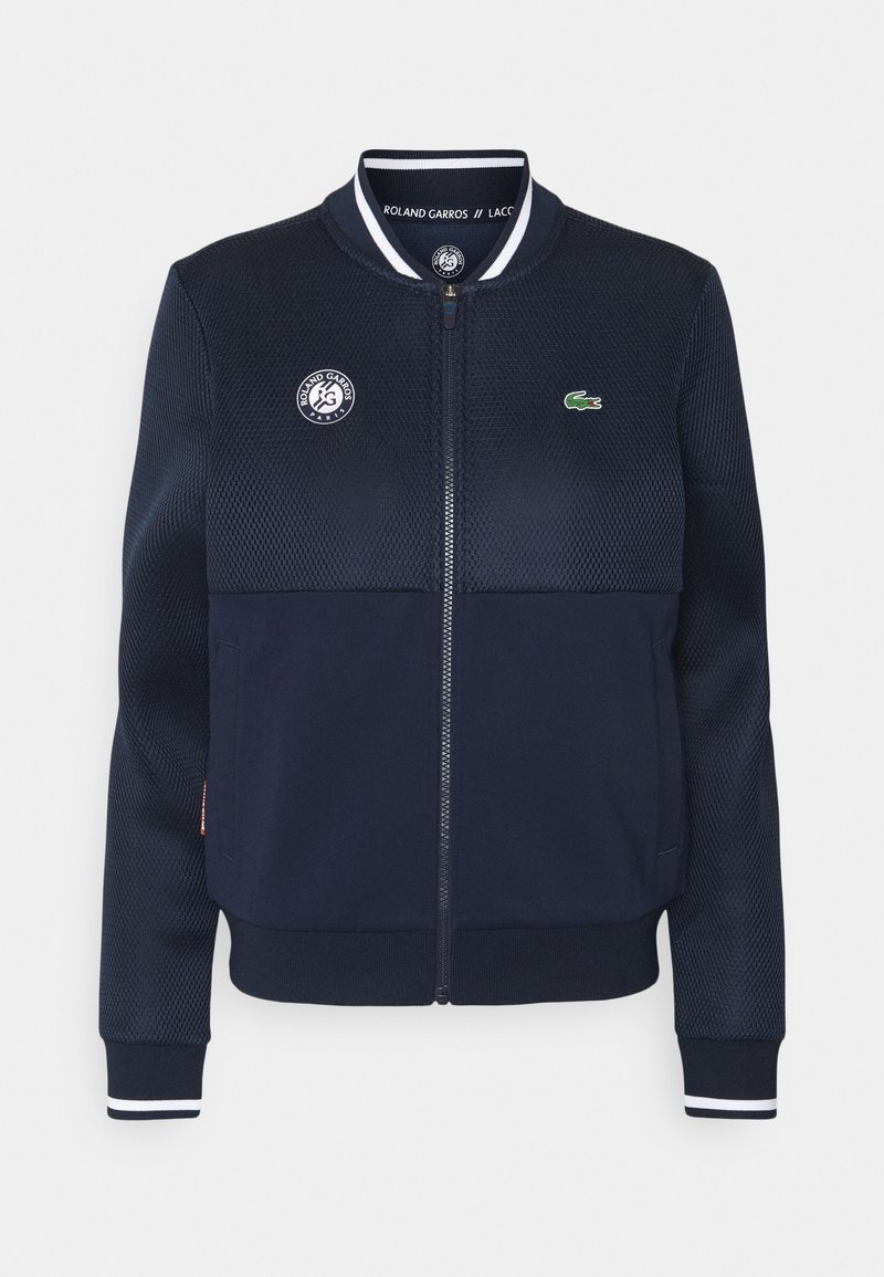 Navy bomber jacket featuring mesh panels, side pockets, and ribbed cuffs. Embroidered logo on chest and striped collar accents. Full zipper.