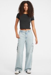 Tricou negru scurt, cu mâneci scurte, asociat cu blugi cargo cu picioare late, de culoare bleu deschis, care au două buzunare laterale și închidere cu buton.