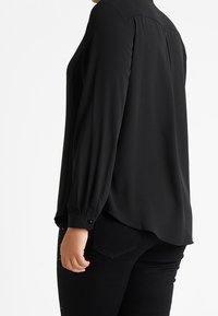 Zwarte blouse met lange mouwen en een kraaglijn, licht gebogen zoom en knoopmanchetten, gemaakt van gladde, lichte stof.
