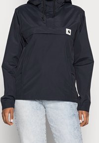 Navy windbreaker with a hood, adjustable drawstrings, front pocket, and logo patch. Features lightweight, water-resistant material.
