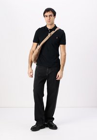 Čierna polokošeľa, voľne strihané čierne džínsy, čierne topánky a béžová crossbody kabelka. Jednoduchý dizajn s malým logom na košeli.