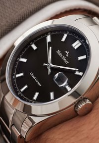 Montre en acier inoxydable argenté avec un cadran noir, des index horaires blancs et une fenêtre de date. Présente une lunette lisse et un bracelet classique.