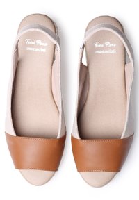 Zapatos slip-on de tela beige con una puntera de cuero marrón y un interior suave. Con los lados abiertos, suela plana y detalles de costura mínimos.